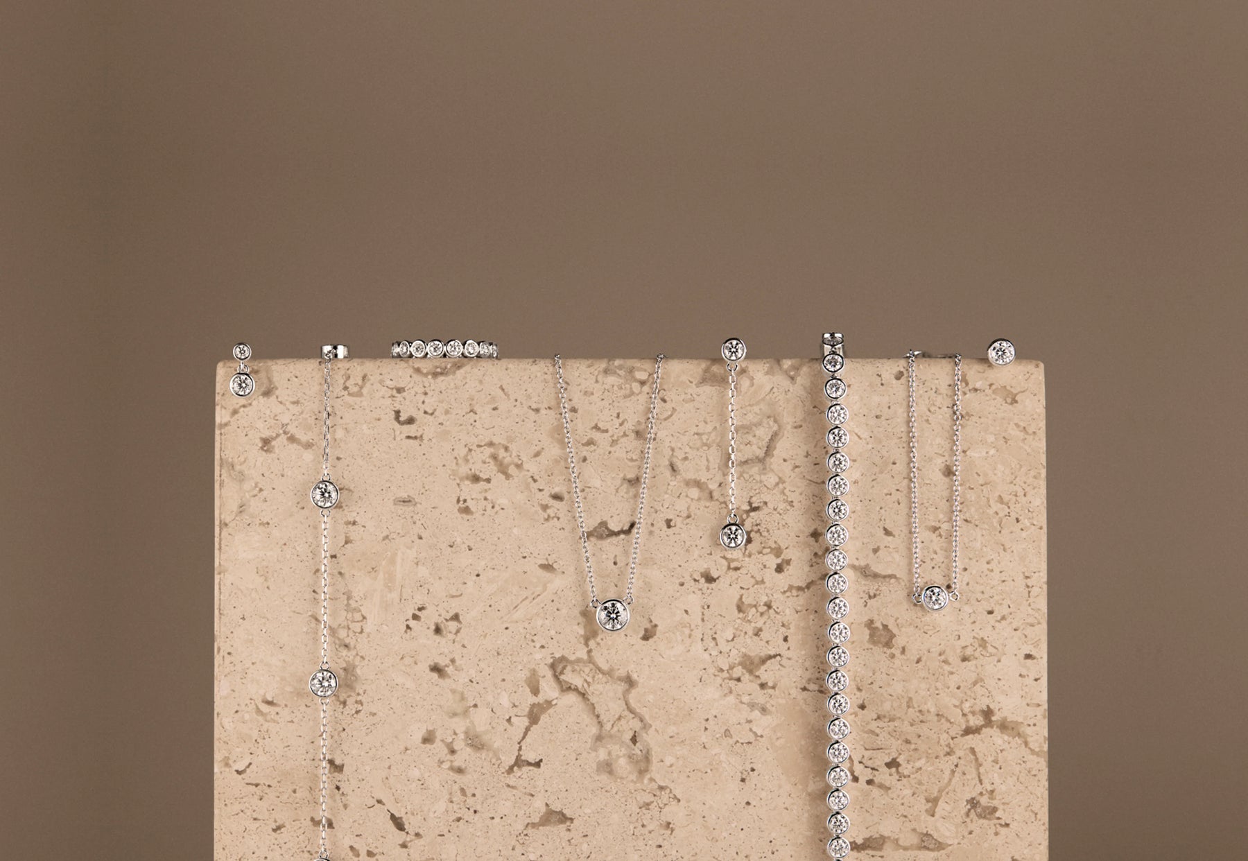 Set of silver necklaces on a textured beige surface with a brown background