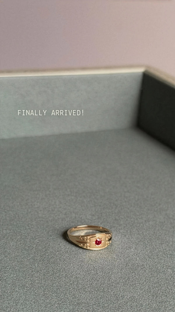 Gold ring with a red gemstone on a gray surface, text 'FINALLY ARRIVED!' above.